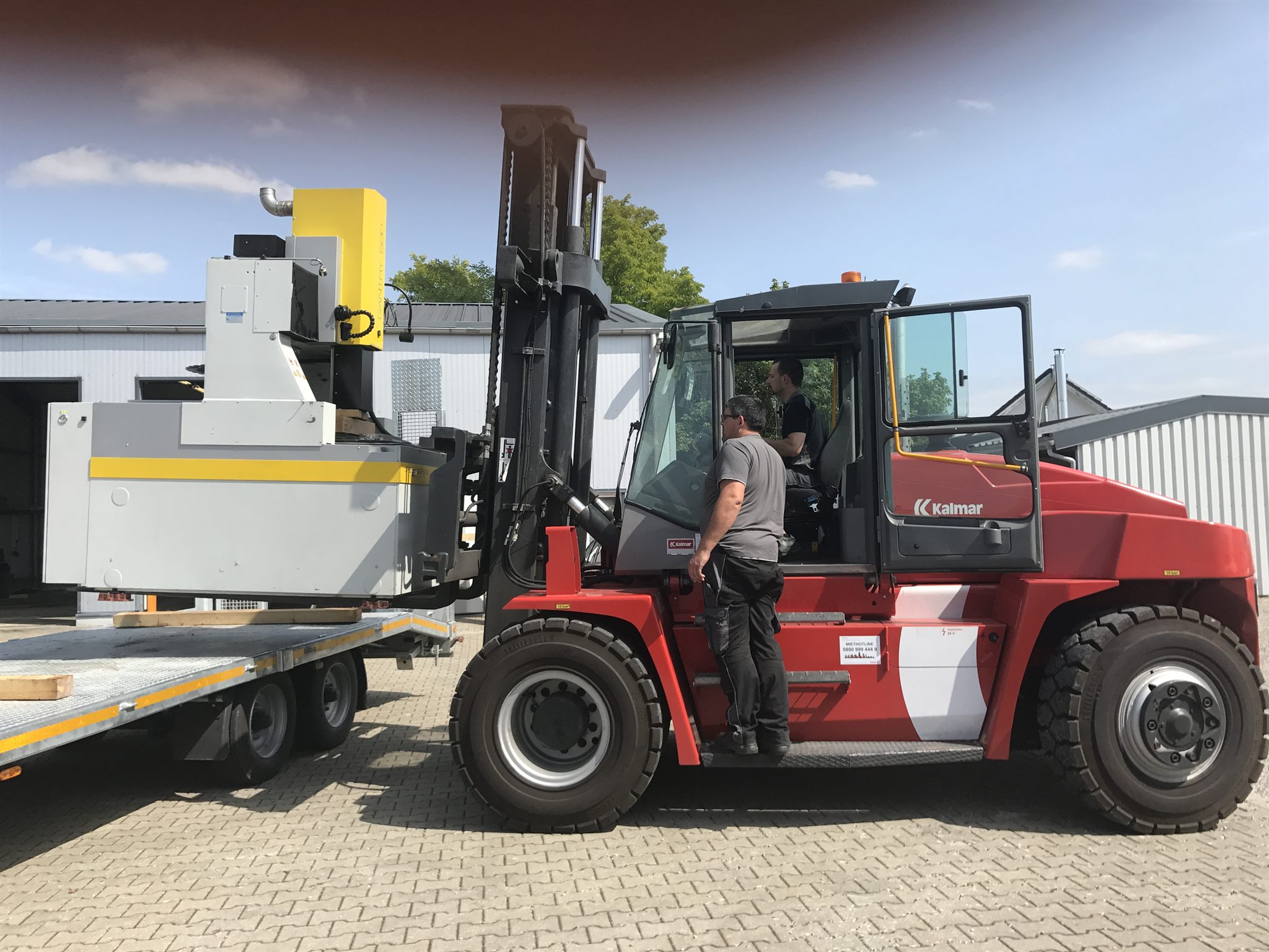 Schwerlaststapler setzt eine Anlage vor der neuen Halle ab, zwei Mitarbeiter dabei