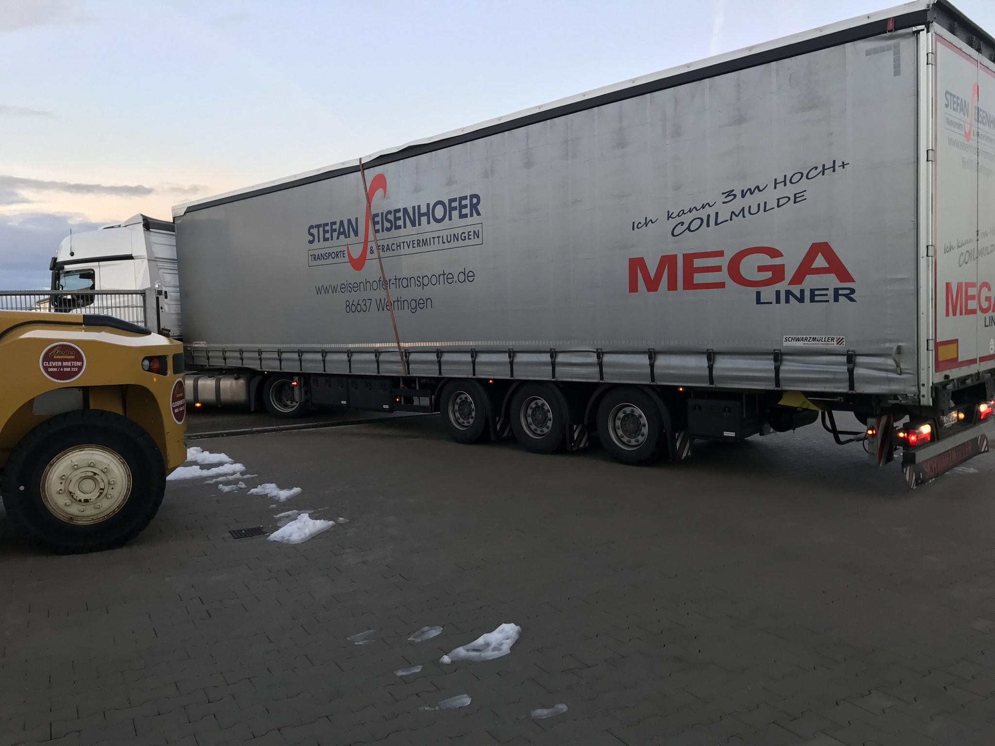 Der Sattelzug mit der C1200V steht im Morgengrauen vor der Halle, Schnee auf dem Hof