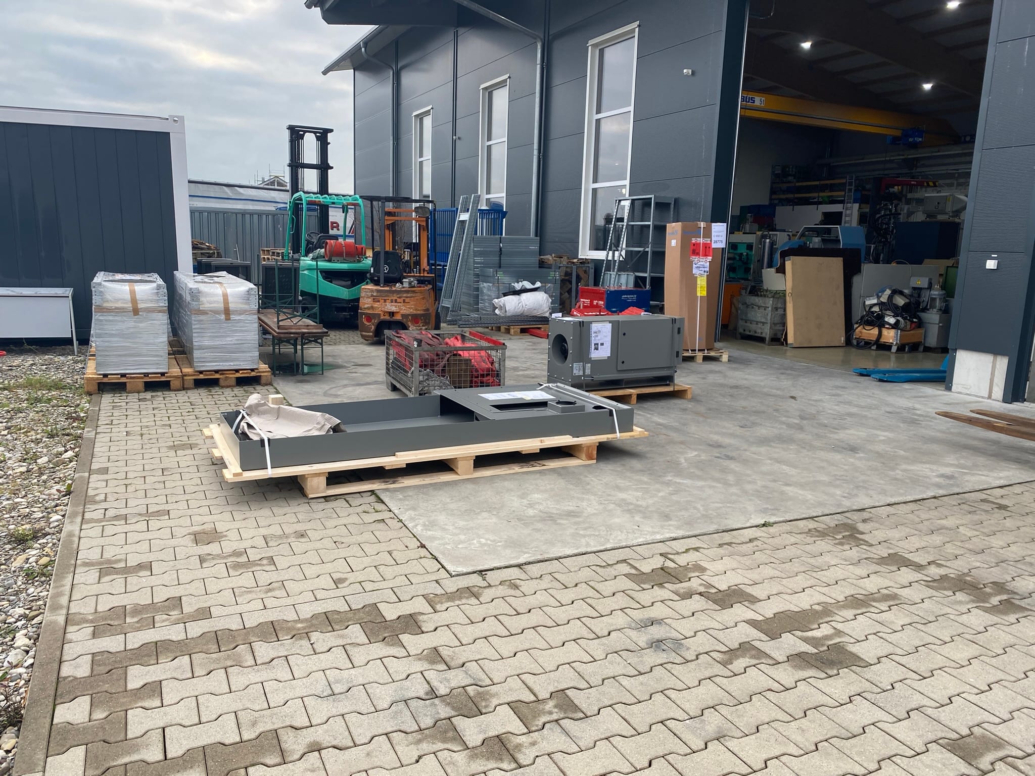 Späneförderer, Kühlaggregat und weitere Anbauteile stehen auf Paletten neben der Halle