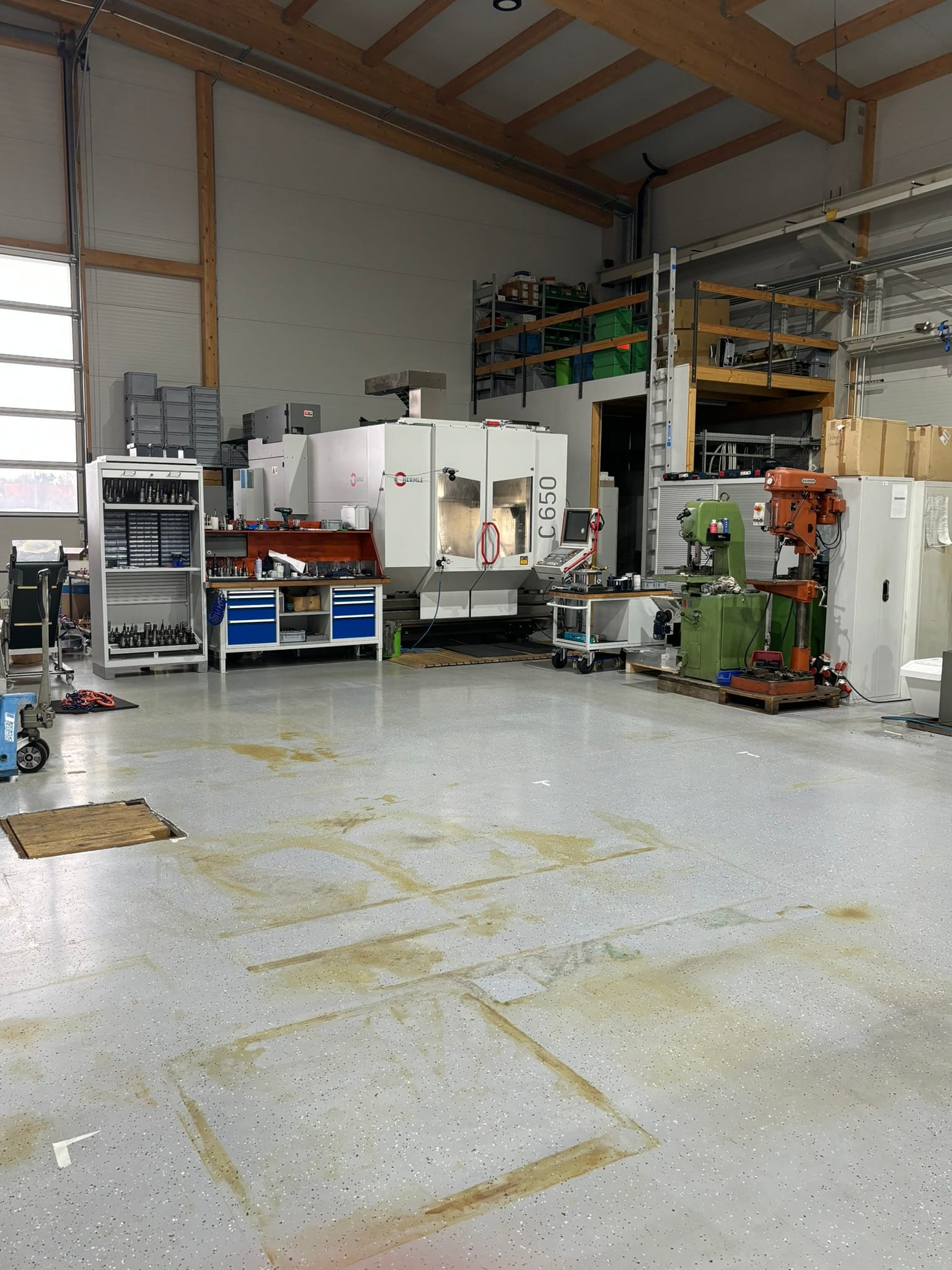 Weiter Blick über den leeren Hallenboden, im Hintergrund die C650U, die Werkbank und die Ständerbohrmaschine