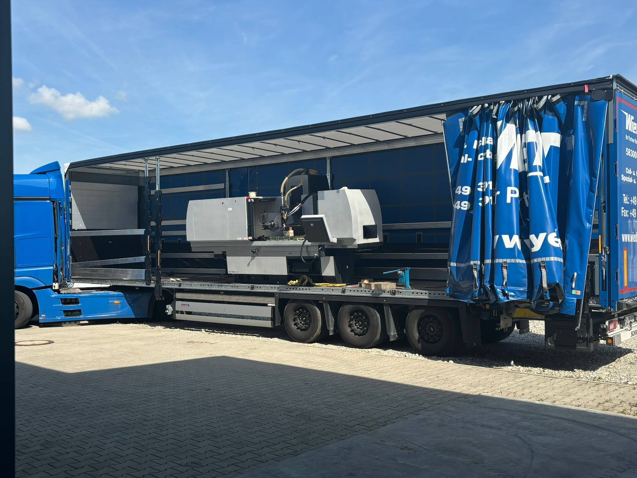 Der offene Planenauflieger vor der Halle, die Schleifmaschine steht quer auf der Ladefläche