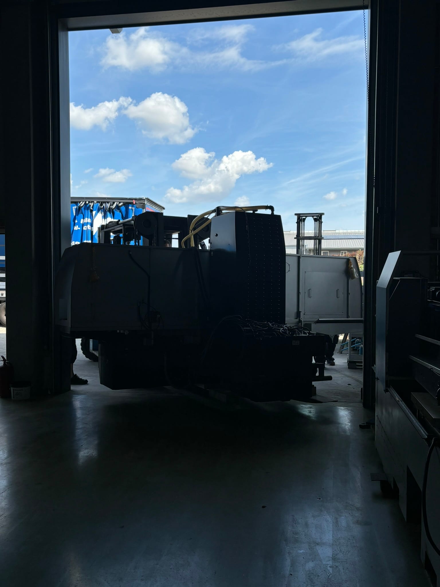 Aus der dunklen Halle durch das offene Tor gesehen: die Maschine im Gegenlicht auf dem Weg herein