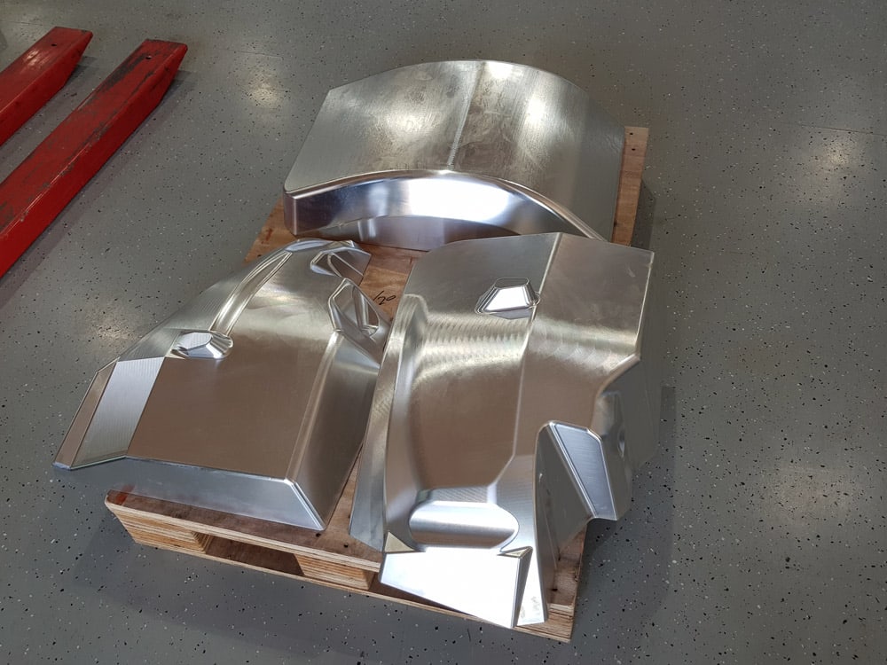 Drei große gefräste Aluminiumteile mit gewölbten Flächen, gestapelt auf einer Palette