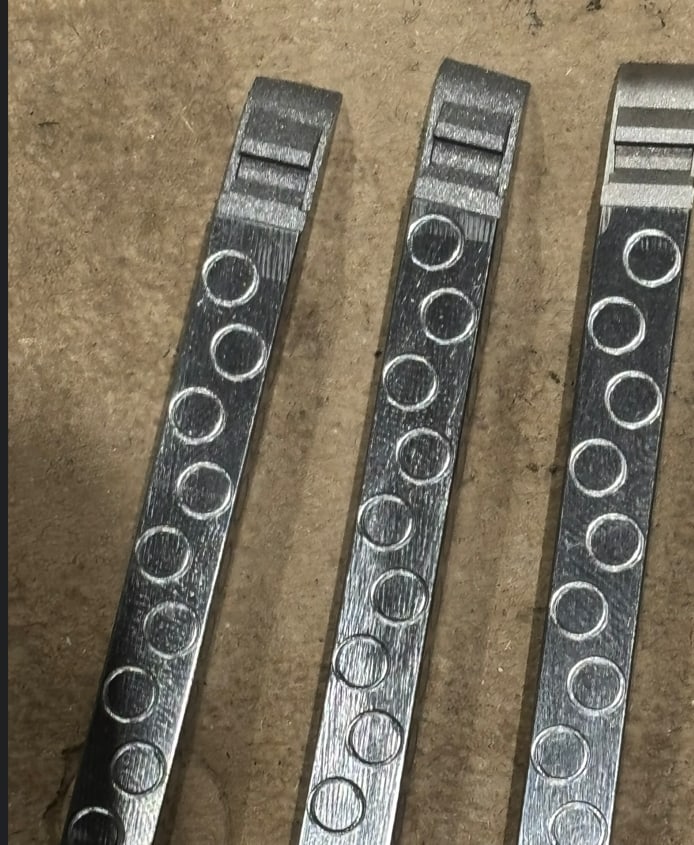 Drei gleiche Metallleisten nebeneinander, jede mit einer Reihe eingebrachter Bohrungen