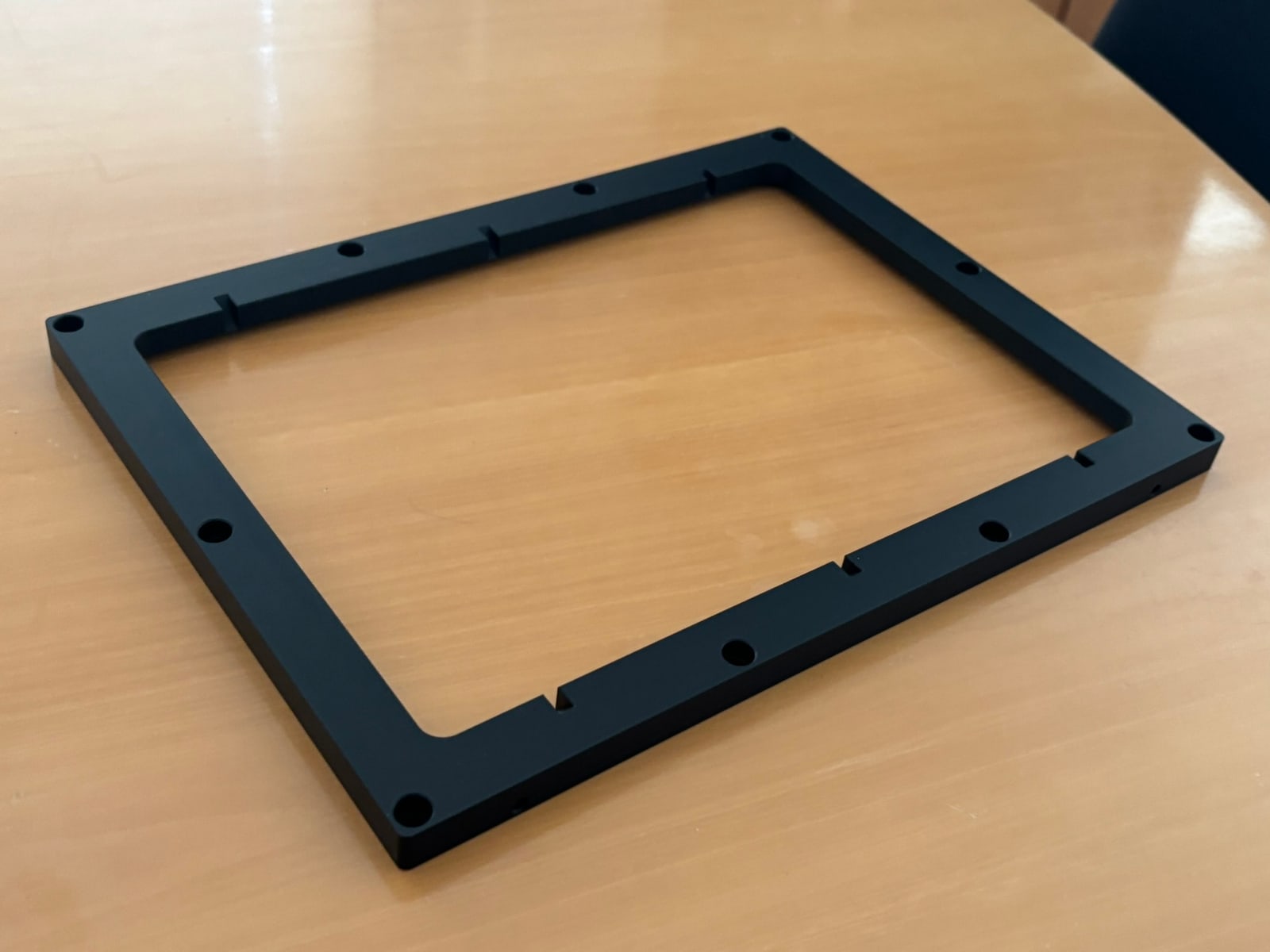 Schwarz eloxierter Aluminiumrahmen mit Befestigungsbohrungen und Aussparungen, schräg von oben